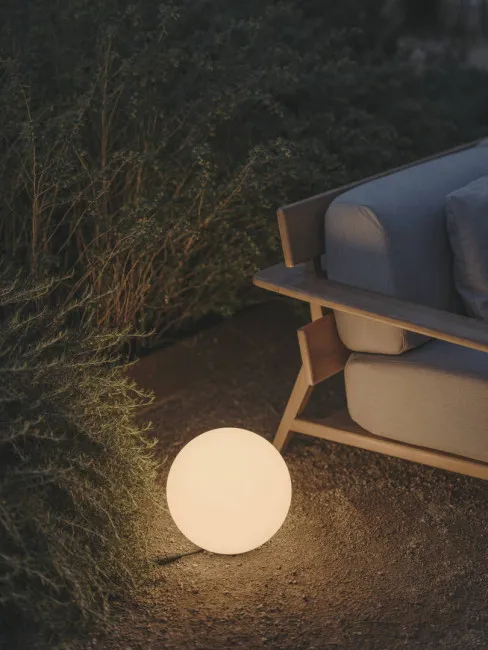 A glowing orb light beside an outdoor sofa at dusk, with plants in the background.