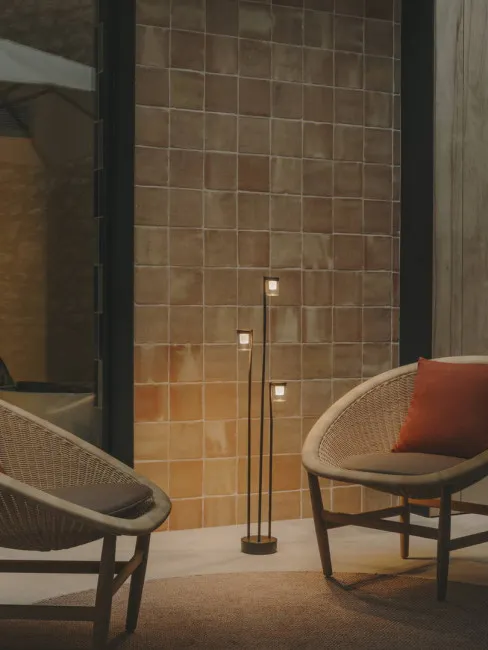 Interior with two wicker chairs, a floor lamp, and a tiled wall.