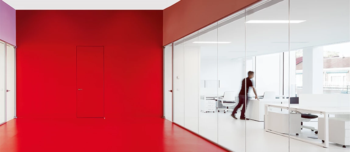 A vibrant office space featuring red and purple decor, complemented by bright white walls and large windows for natural light.
