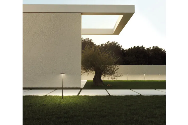 Modern architecture with an overhanging rectangular structure, a tree, and path lights by a reflective pool at dusk.