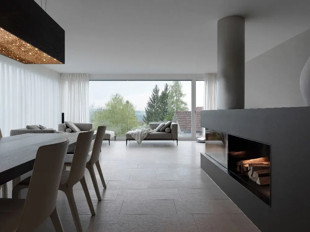 A cozy modern dining room featuring a fireplace and a large window, inviting warmth and natural light into the space.