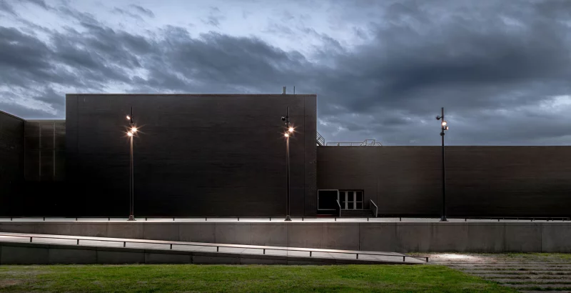 Modern building with street lamps at dusk, under a cloudy sky.