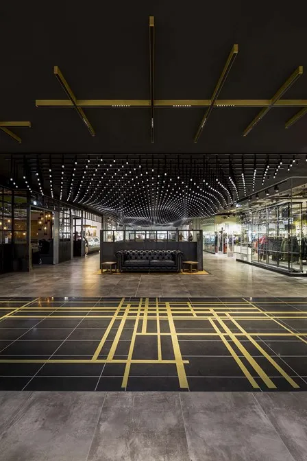 Modern interior with geometric lighting, dark ceilings, golden floor lines, and a central black couch.