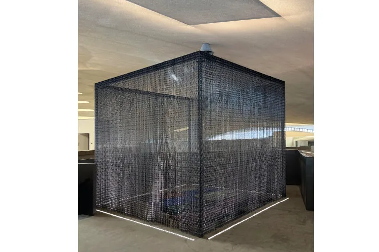 Mesh enclosure in an office space with subdued lighting.