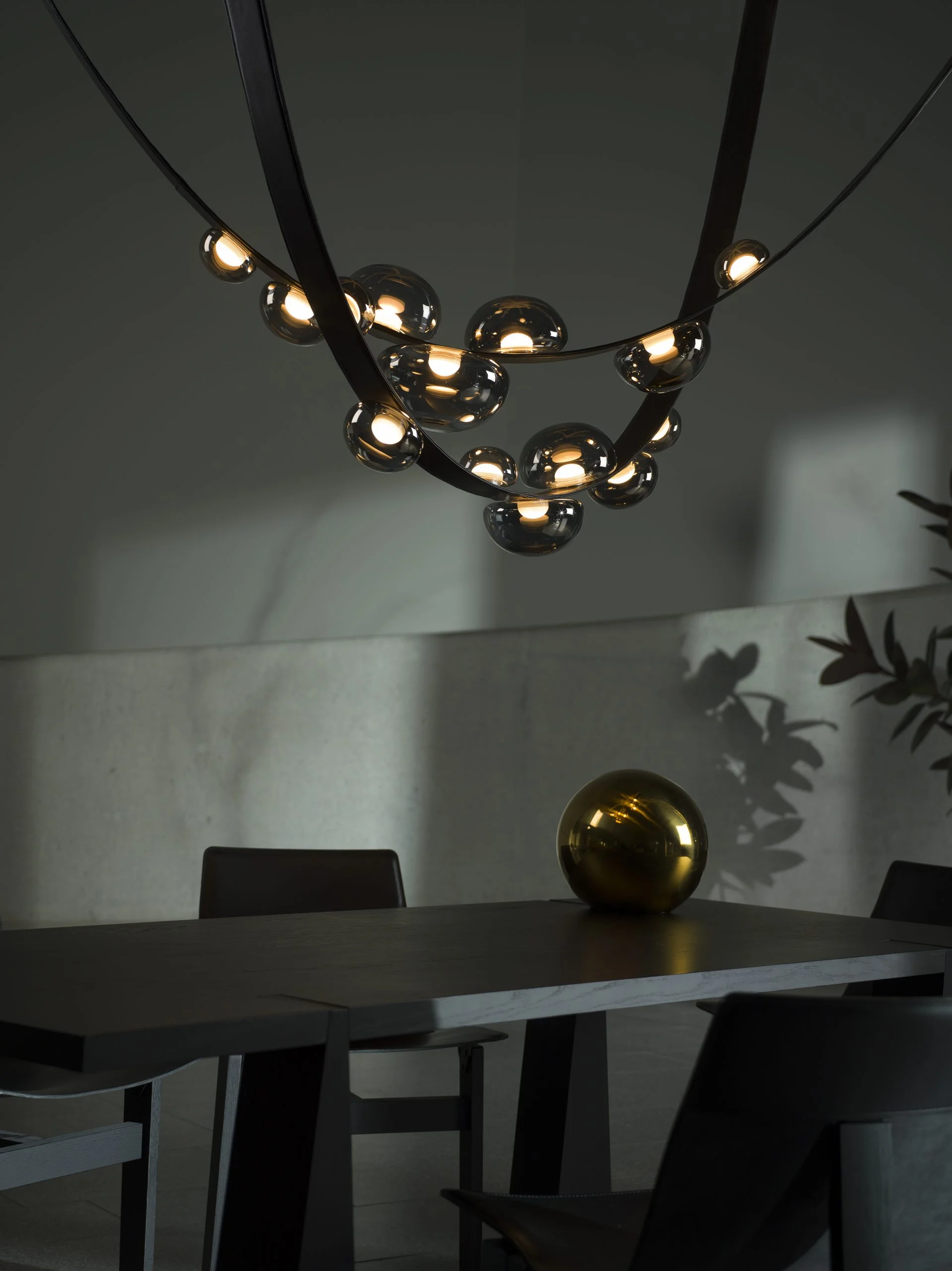 A modern chandelier above a dark dining table with a golden sphere as décor.