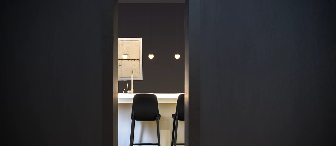 A modern kitchen viewed through a doorway with two chairs and pendant lights.