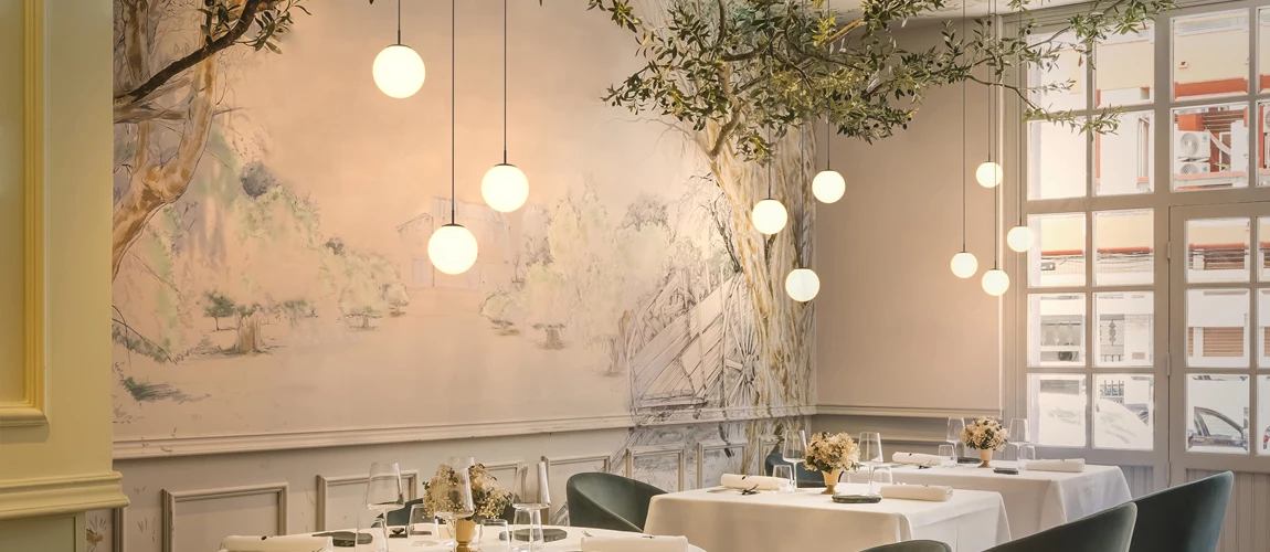 Elegant dining room with mural walls, hanging orb lights, and set tables by a window.