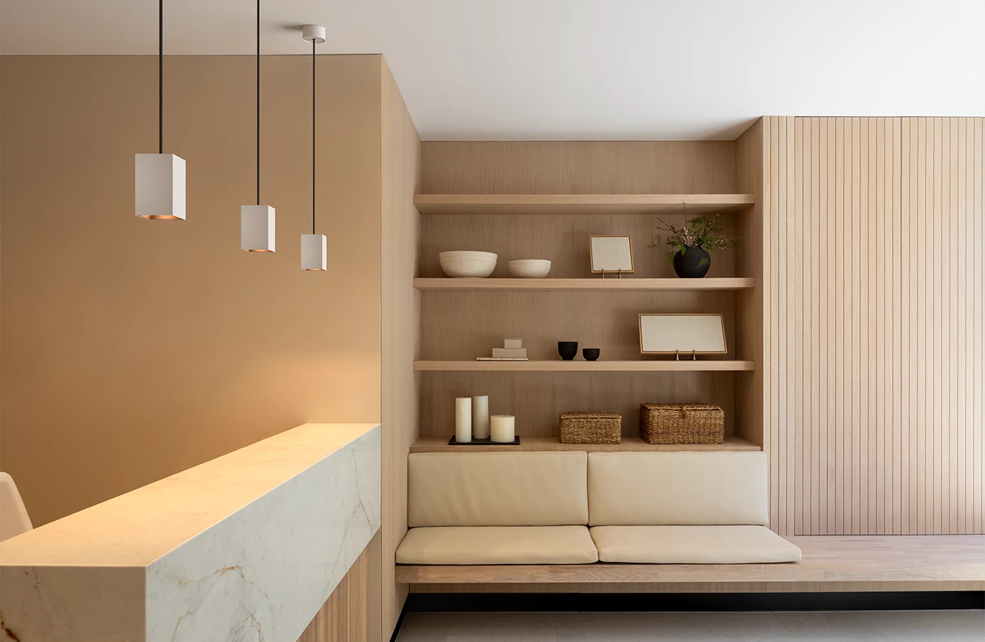 Modern interior with beige built-in bench, wooden shelves, pendant lights, and marble countertop.