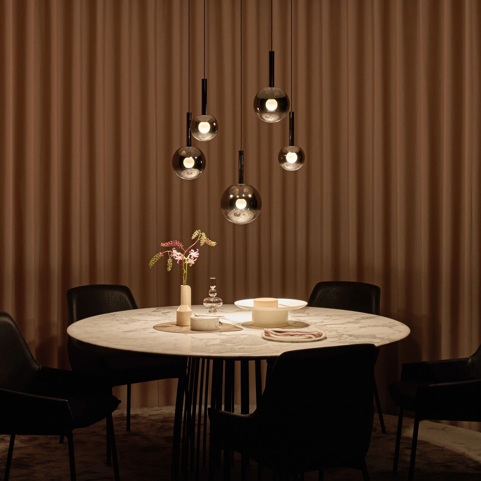 Elegant dining setup with marble table, black chairs, and modern spherical pendant lights.