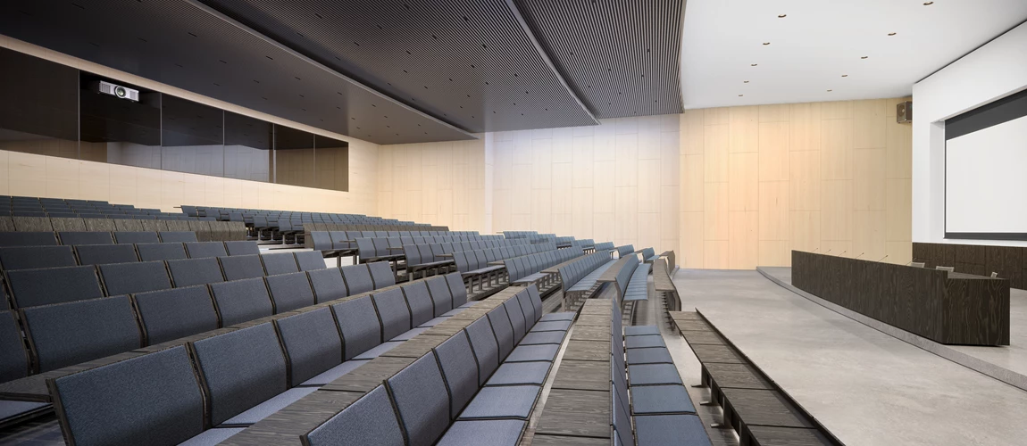 A spacious auditorium featuring blue seats arranged in rows, with a large projector screen at the front for presentations.