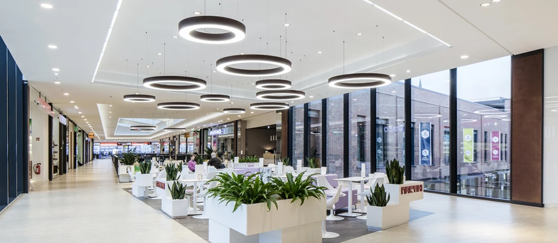 Modern mall interior with circular hanging lights, white seating areas, and large windows.